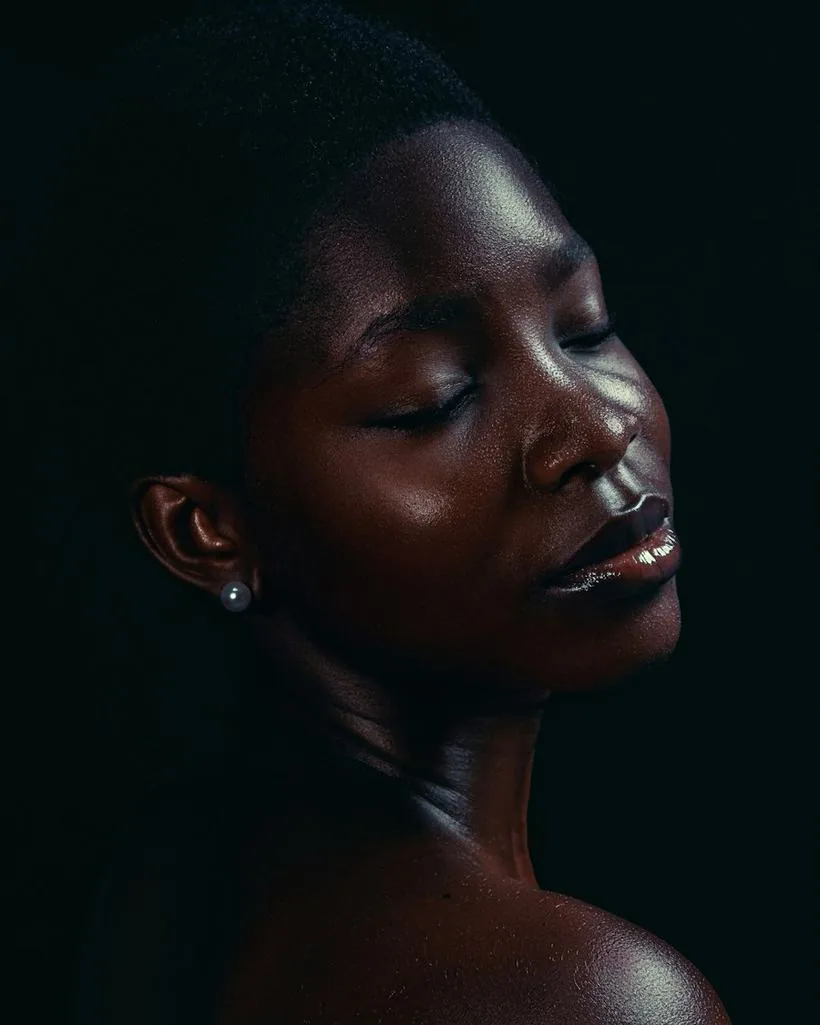 A woman with glowing skin and eyes closed, lit softly against black